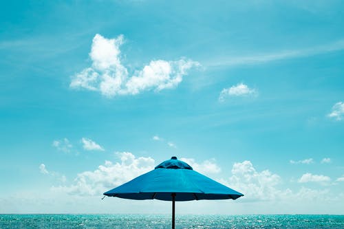 在蓝天下的水附近的蓝色阳伞的特写照片 · 免费素材图片