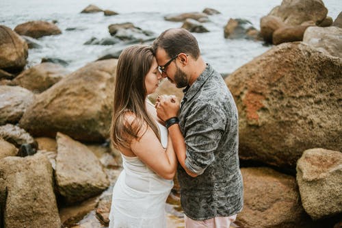 夫妇站在水边的岩石上时互相抱着的照片 · 免费素材图片