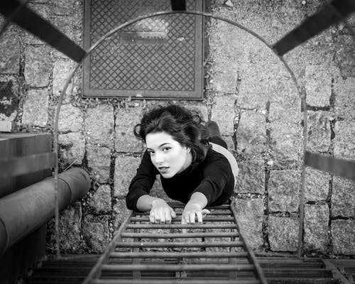一个女人要爬走火梯的灰度照片 · 免费素材图片