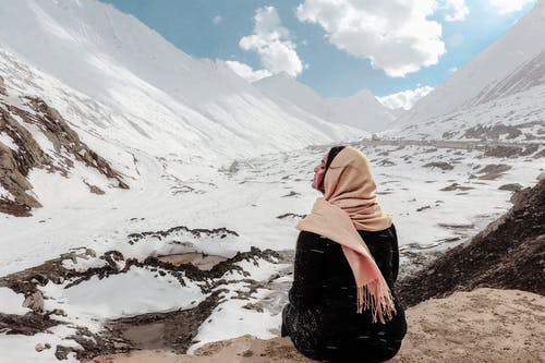 黑色礼服的女人坐在岩石上被雪覆盖的山谷 · 免费素材图片