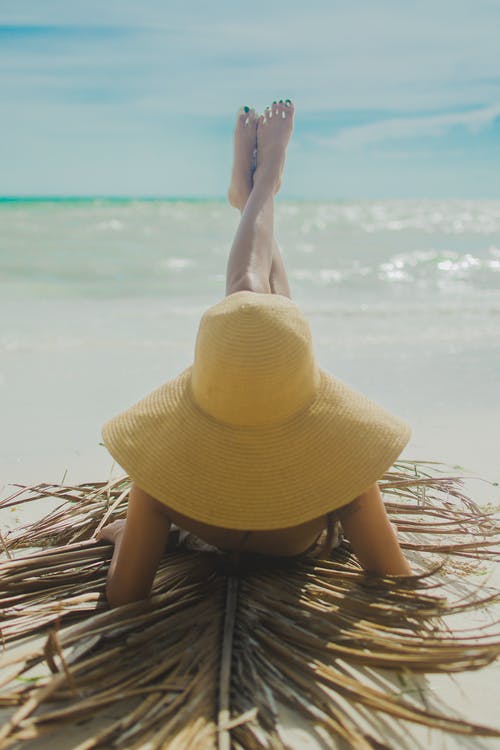 女人戴着黄色帽子的脚抬起岸上晒日光浴 · 免费素材图片