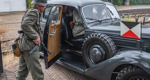 穿着旧军服的男人的照片，步枪站在士兵里面的老式军车 · 免费素材图片