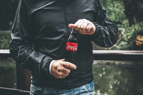 拿着瓶可口可乐的黑夹克的人 · 免费素材图片