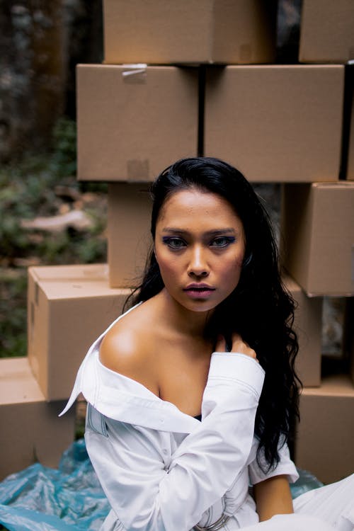 坐在堆积的棕色纸板箱前的女人 · 免费素材图片