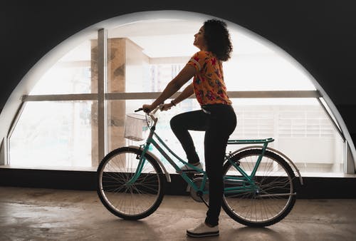 女人坐在拱窗边建筑物内的自行车 · 免费素材图片