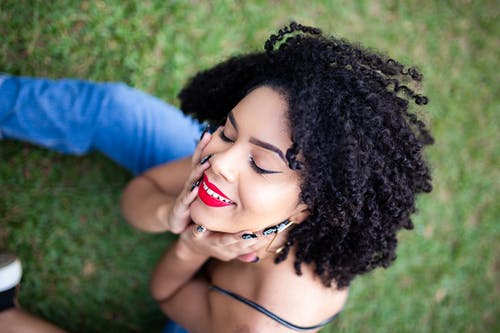 微笑的女人坐在草地上，她闭上眼睛摆姿势的特写照片 · 免费素材图片