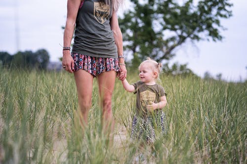 女人站和握着婴儿的手在绿色的田野附近 · 免费素材图片