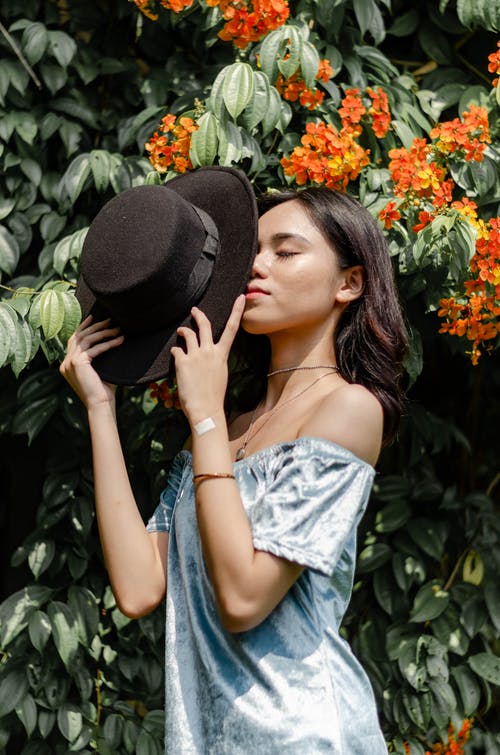 女人拿着橙色的花朵附近的黑帽子 · 免费素材图片