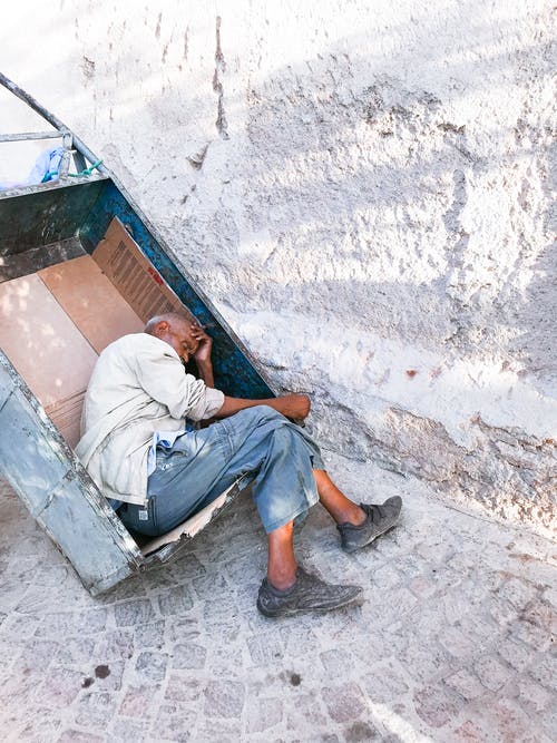 一名老人在靠近墙的街道上的金属车上睡觉 · 免费素材图片