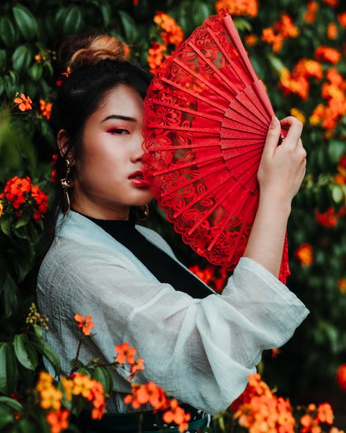 女人拿着花在植物旁边的红色风扇 · 免费素材图片