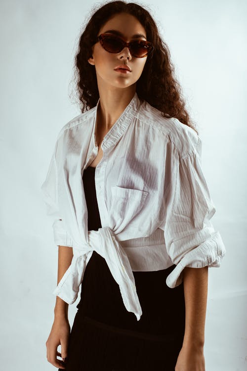 白衬衫，黑色连衣裙和太阳镜摆在白色背景前的女人的照片 · 免费素材图片