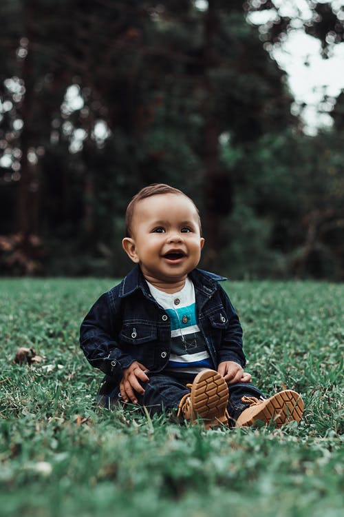 微笑的男婴，牛仔服装坐在草地上的照片 · 免费素材图片
