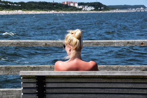 女人坐在水体前的灰色长椅上 · 免费素材图片