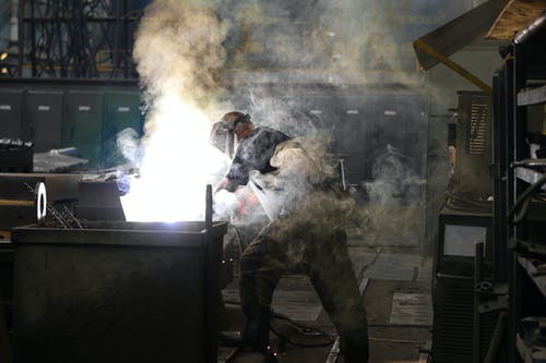 男子戴着电焊烟气中覆盖的焊接面罩 · 免费素材图片
