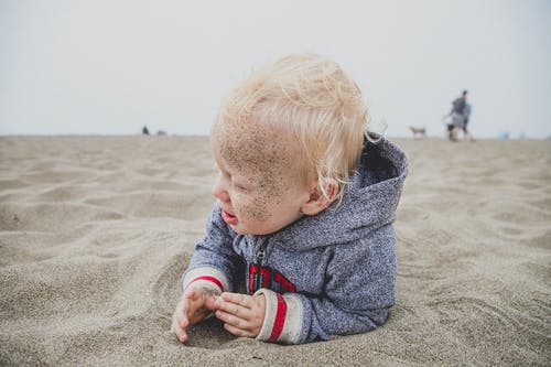 孩子躺在沙滩上，他脸上的沙子 · 免费素材图片