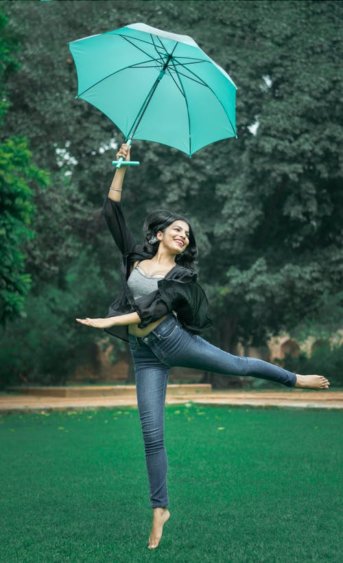 女人在白天跳舞和在草地上养绿色的伞 · 免费素材图片