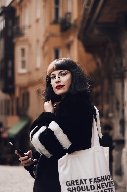 黑色和白色外套，背着手提袋的常设女人的选择性焦点侧视图照片 · 免费素材图片