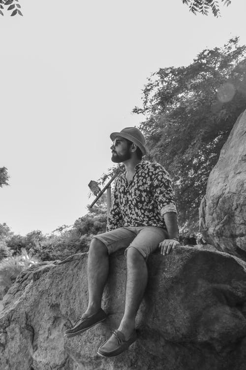 人坐在岩石戴着帽子和墨镜的灰度摄影 · 免费素材图片