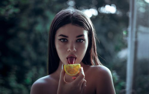 女人舔橙色水果的选择性焦点摄影 · 免费素材图片