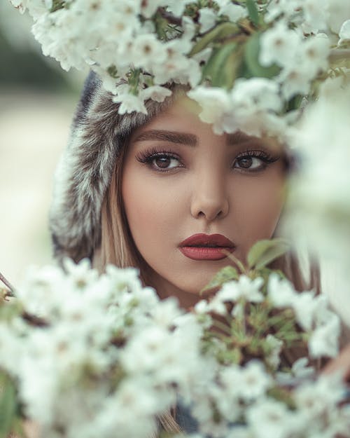 白花背后的女人的脸的特写照片 · 免费素材图片
