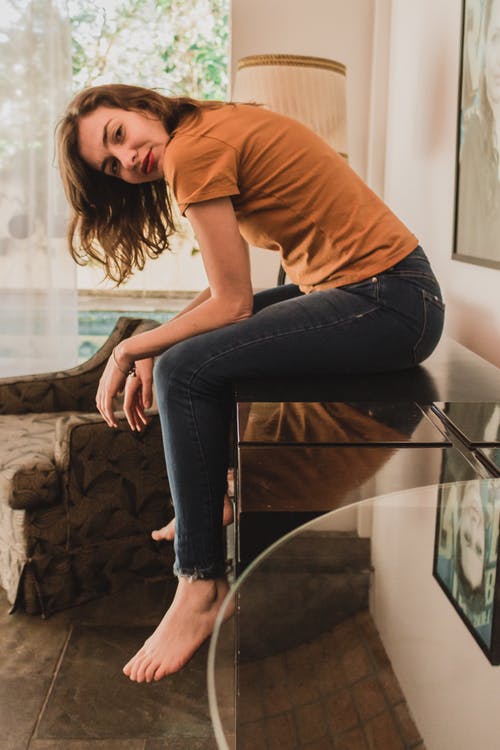 穿棕色t恤和牛仔牛仔裤，坐在木桌上的女人的照片 · 免费素材图片