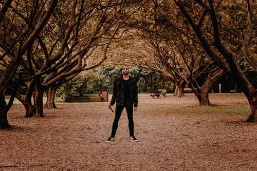 一个拿着太阳镜的人的照片站立在树下在公园 · 免费素材图片