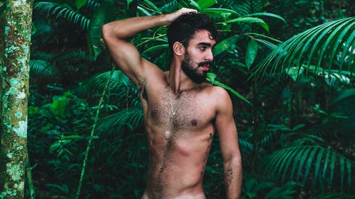 裸照的男人站在绿色的植物附近，用手在他的头上 · 免费素材图片