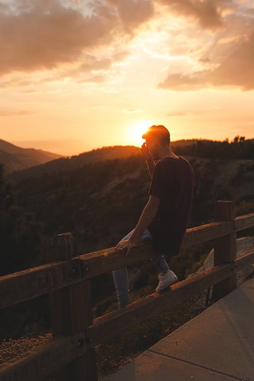 男子在黎明时坐在木栅栏上的照片 · 免费素材图片