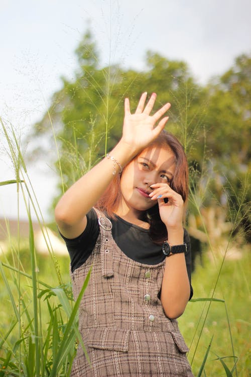 女人站在草地上遮住她的脸从阳光 · 免费素材图片