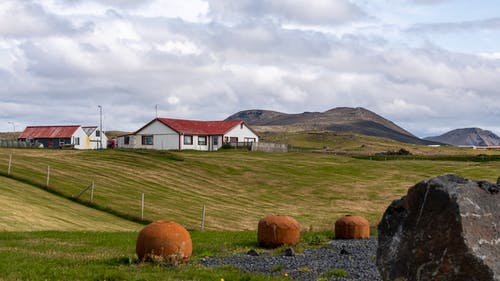 山脉包围农田的白色和棕色房子 · 免费素材图片