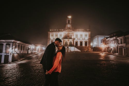 情侣接吻在晚上与背景中的建筑物的照片 · 免费素材图片