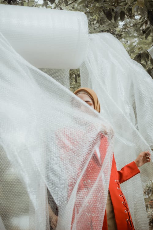 女人穿着橙色的长袖衬衫，拿着泡沫包装 · 免费素材图片