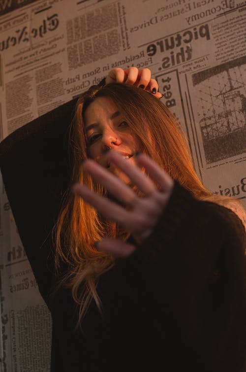黑色毛衣站在她的手与报纸墙附近的女人的照片 · 免费素材图片
