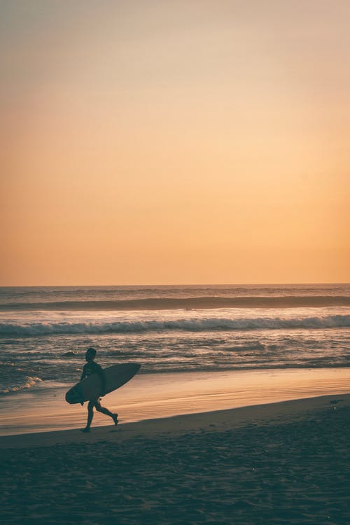 男子在海边携带冲浪板 · 免费素材图片