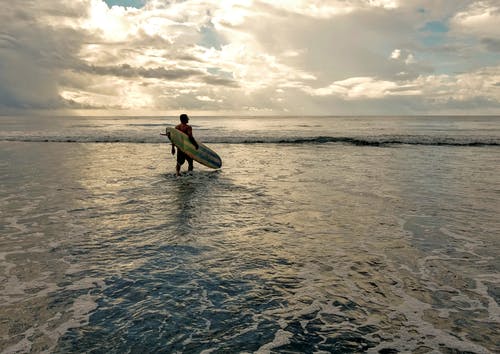 男子手持冲浪板在水面上 · 免费素材图片