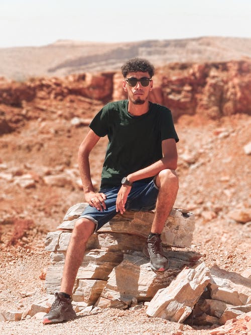 一个穿着黑色圆领t恤坐在岩石上的男人的照片 · 免费素材图片