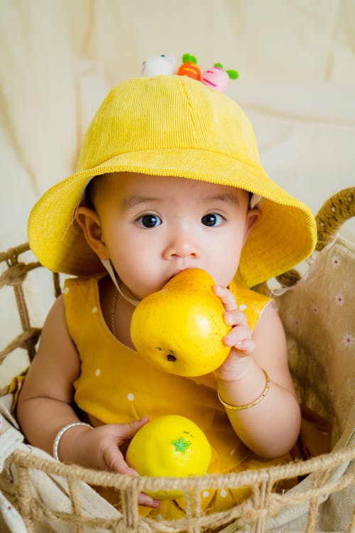 黄色上衣和帽子举行水果蹒跚学步 · 免费素材图片