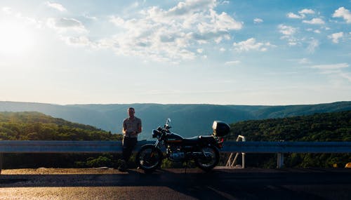 男子倚在摩托车旁边的金属框架 · 免费素材图片