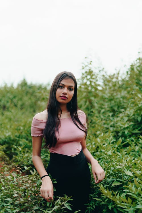 女人穿着粉红色的露肩上衣和黑色的裙子站在绿叶植物附近的照片 · 免费素材图片