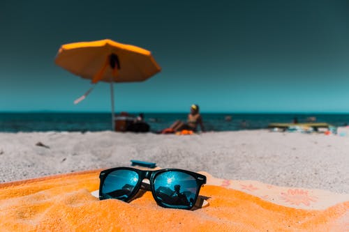 在岸上的棕色毯子上的黑色太阳镜 · 免费素材图片