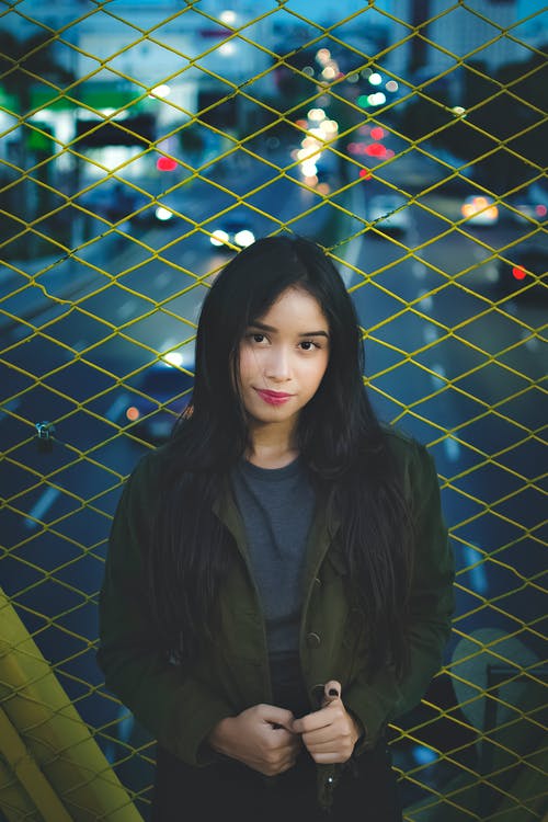 栅栏旁边的橄榄绿色外套的女人 · 免费素材图片