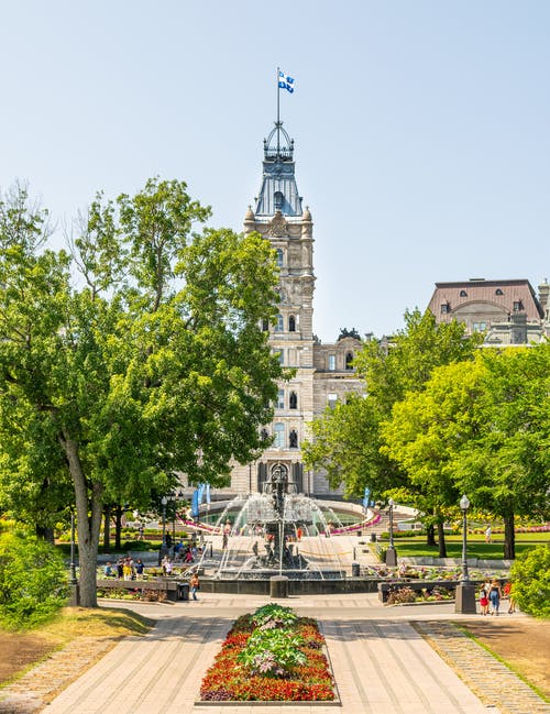 人们用喷泉在公园里的人行道上包围着树木和花草，在一座带有塔的建筑物前 · 免费素材图片