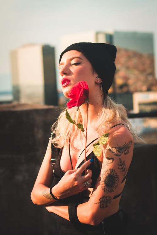 黑色衣服和无檐小便帽帽子拿着红色的花的纹身女人的选择性焦点照片 · 免费素材图片