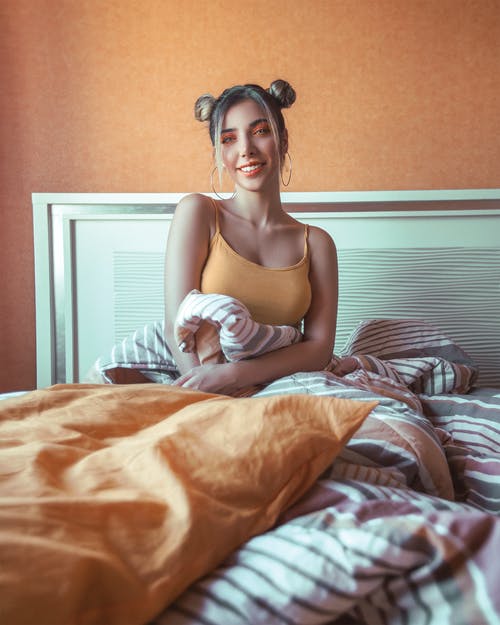 坐在床上的橙色意大利面条皮带顶部的微笑女人的照片 · 免费素材图片