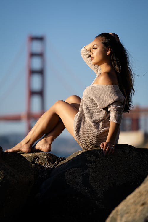 女人穿着灰色毛衣坐在岩石上 · 免费素材图片
