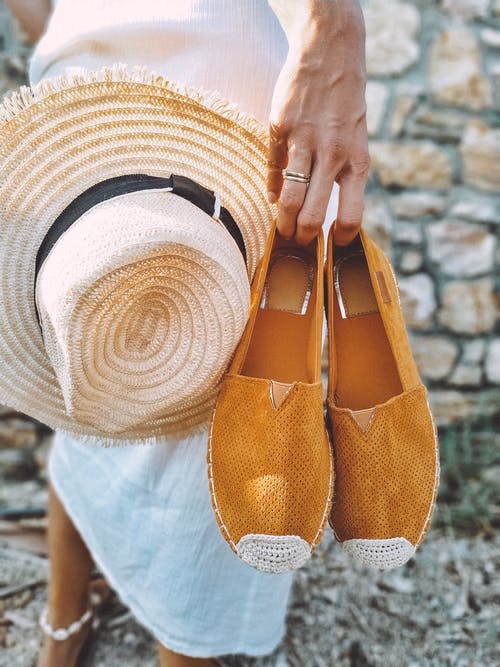 女人拿着棕色的帆布鞋和棕色的太阳帽子的选择性聚焦摄影 · 免费素材图片
