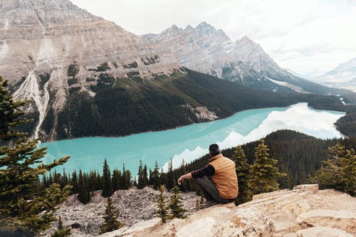 穿棕色背心，坐在山上看着湖的人 · 免费素材图片