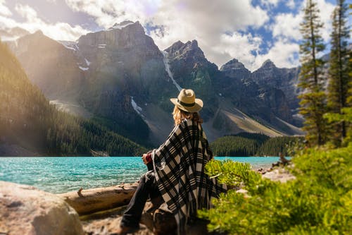 一个女人坐在湖边的一块岩石上 · 免费素材图片