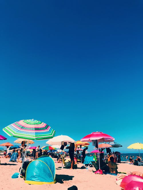 人们坐在沙滩遮阳伞下站着 · 免费素材图片
