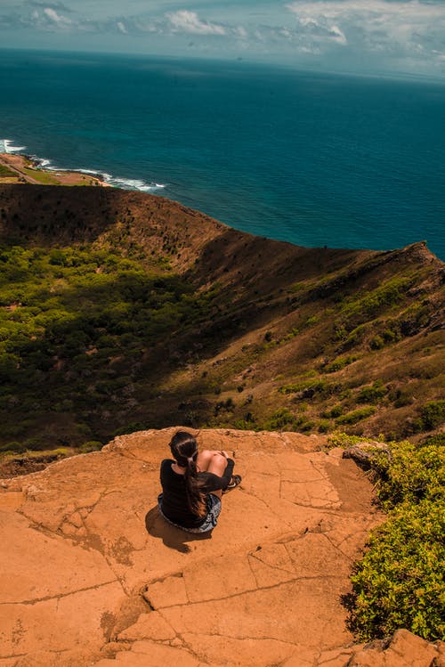 女人坐在悬崖上，看着大海 · 免费素材图片